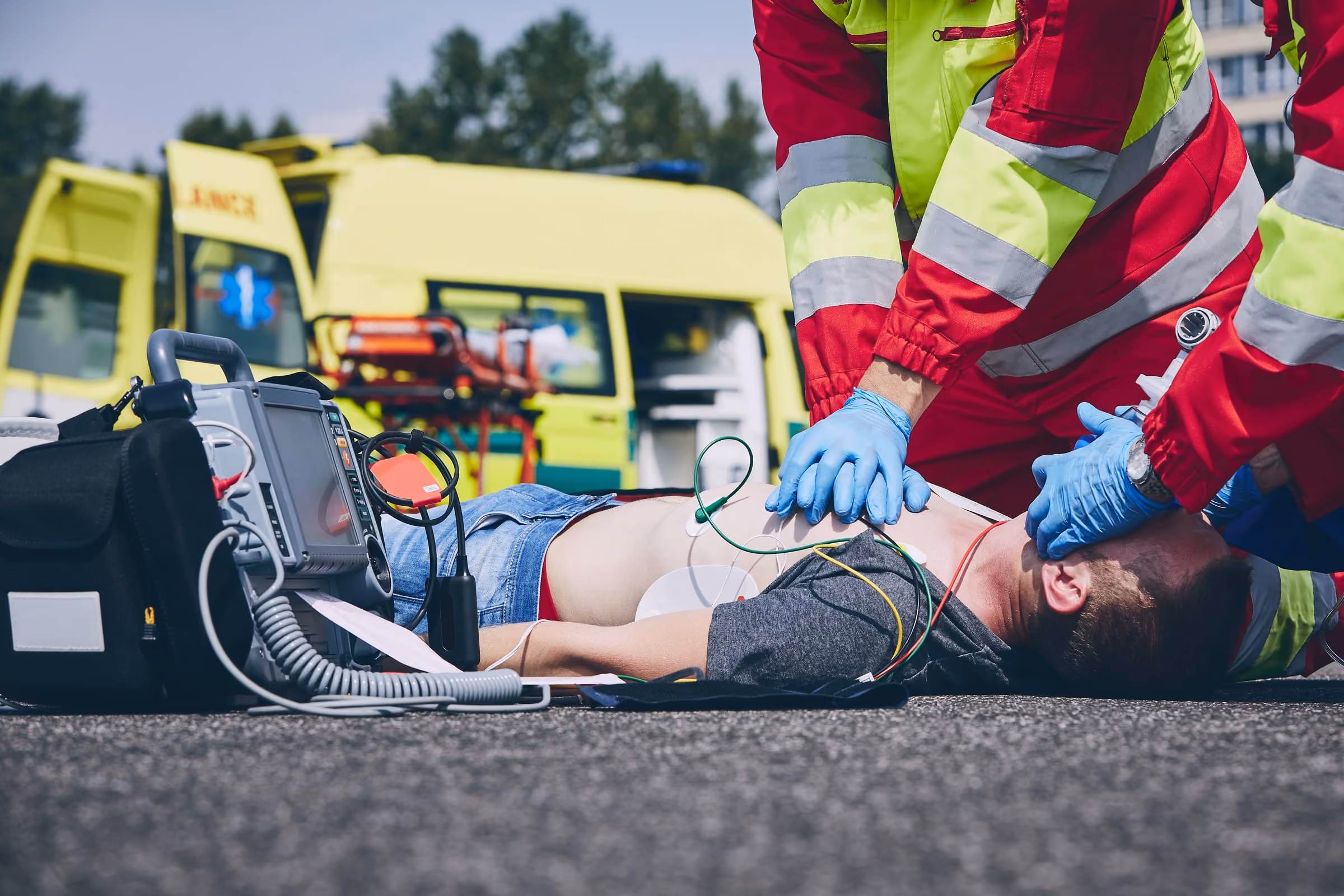 Des ambulanciers pratiquent un massage cardiaque à côté d'une ambulance, avec un défibrillateur
