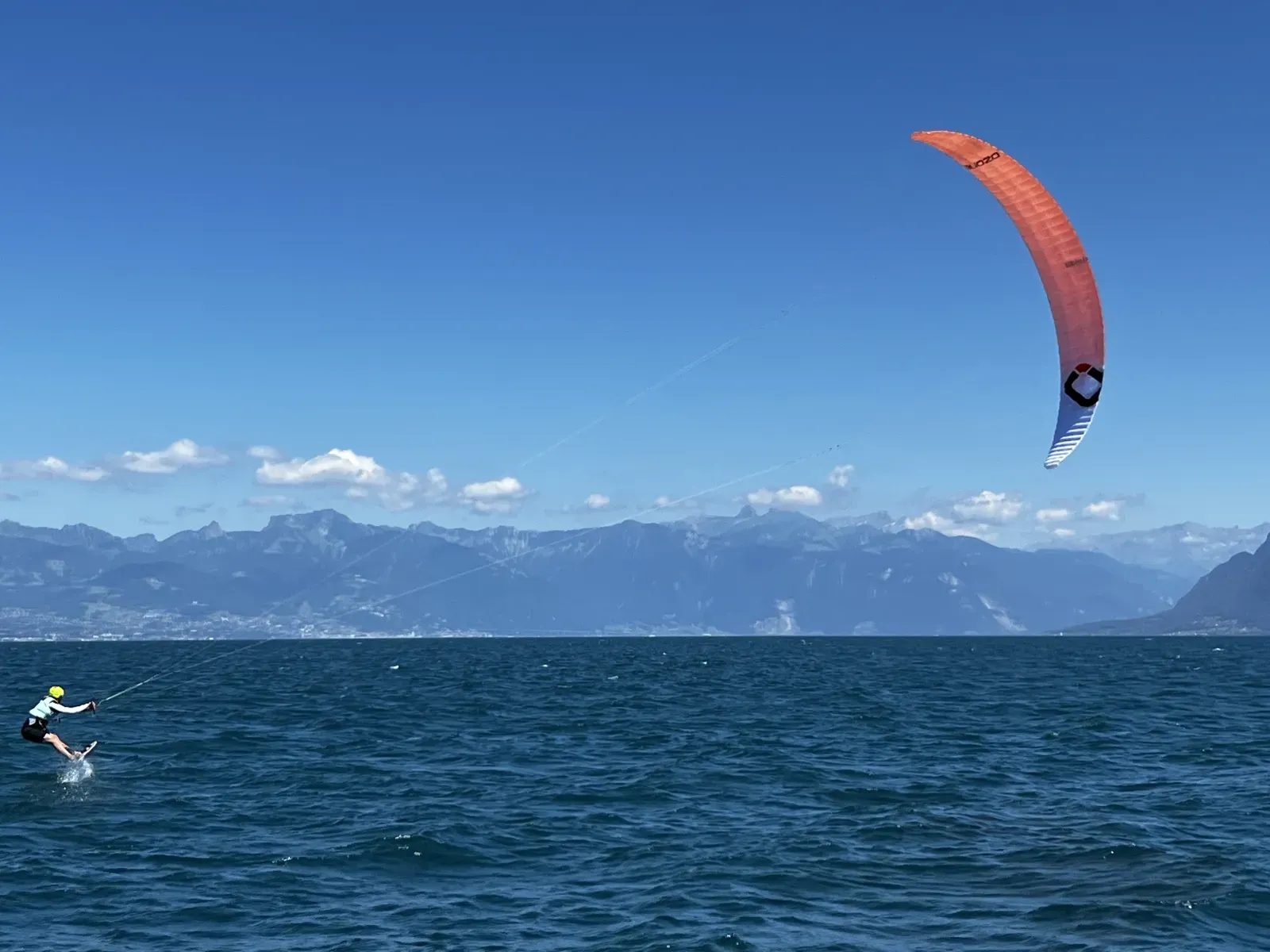 Un kitefoiler sous aile orange file sur le Haut-Lac, les Alpes en arrière-plan