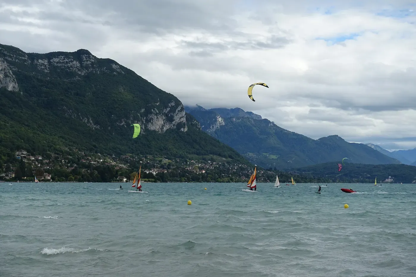 Kitesurfeurs et véliplanchistes sur un lac de montagne, bouées jaunes au premier plan