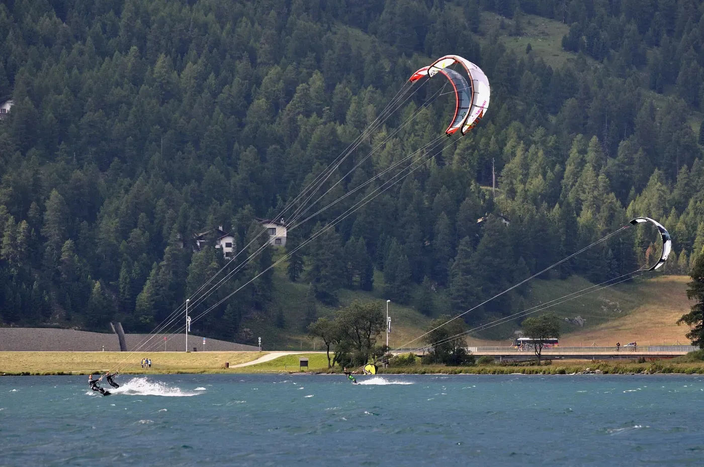 Un kitesurfeur glisse près du rivage, son aile blanche et rouge tendue au-dessus de la forêt