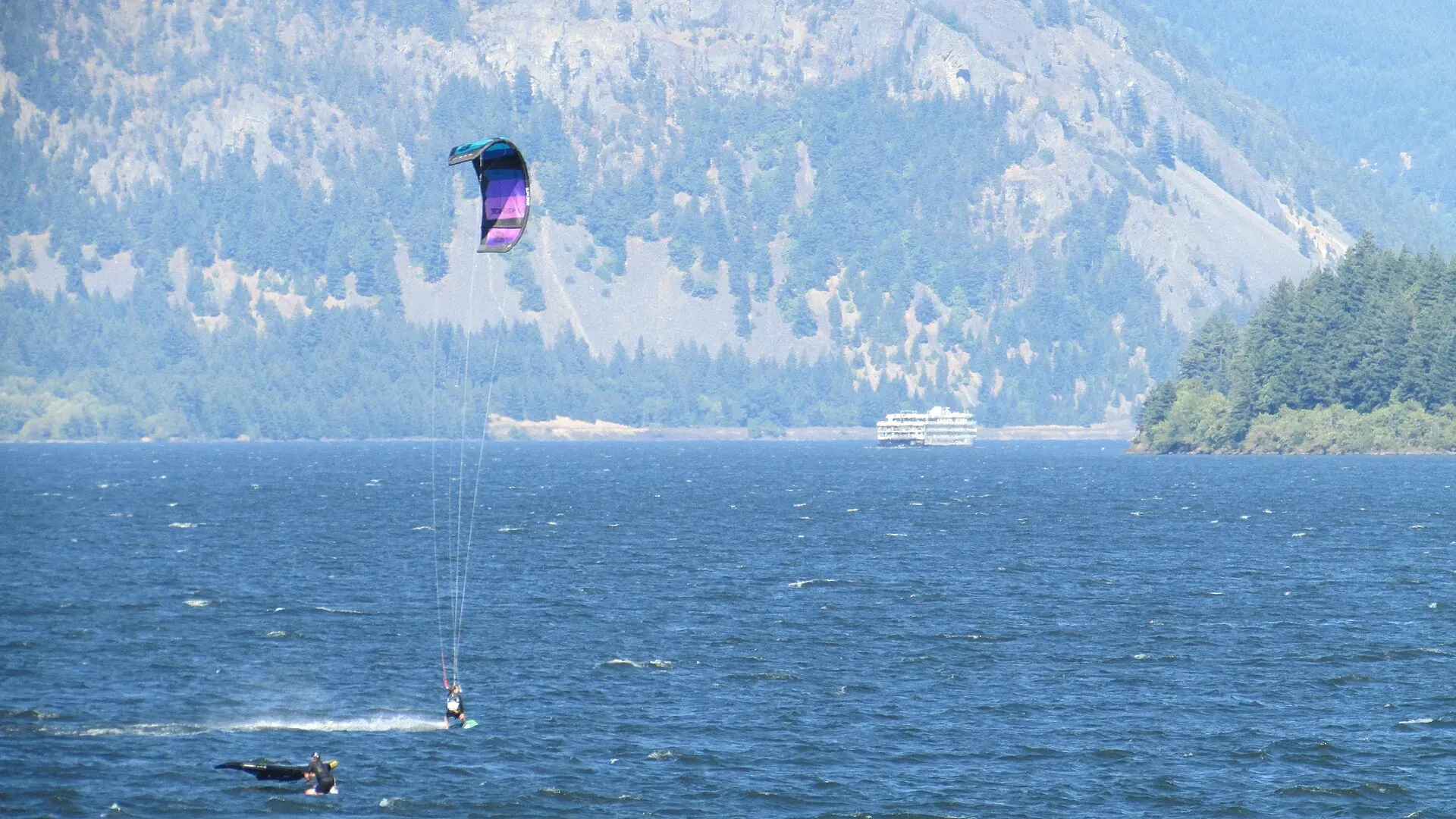 Un kitesurfeur sur un grand lac bordé de falaises boisées